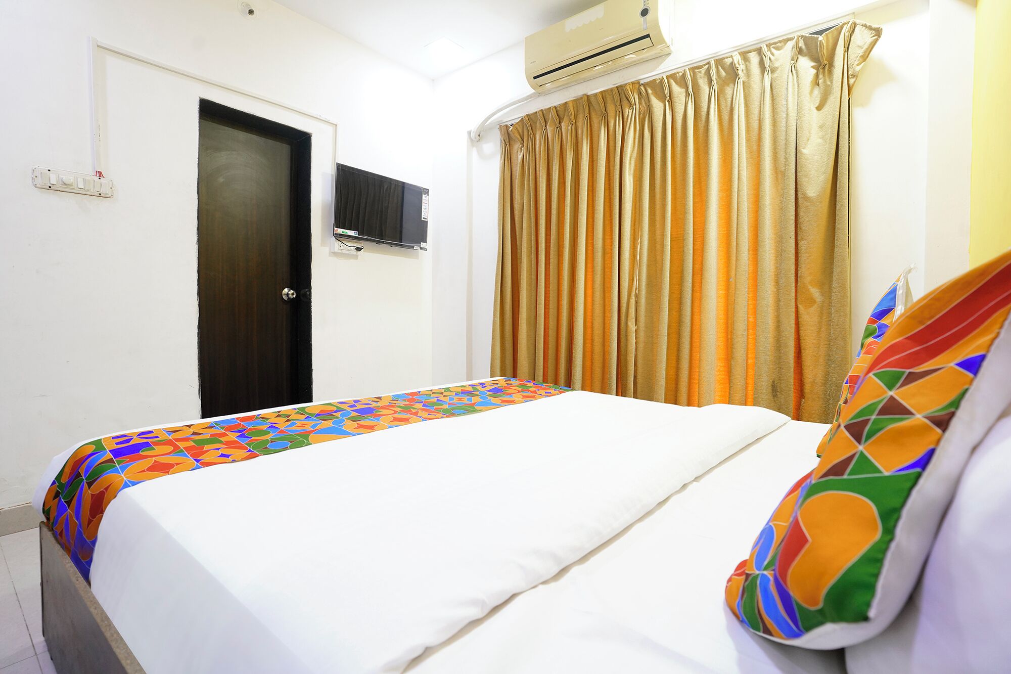 A hotel room with a bed, a door, an air conditioning unit, and curtains.