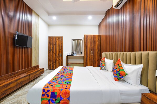 A hotel room with a bed, a television, wooden paneling, a wardrobe, and a desk with a mirror. - FabHotel Regal (Mohali)