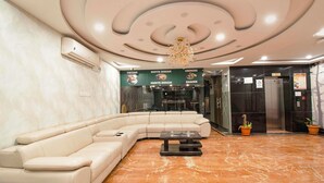 A modern lobby with a sectional sofa, a marble floor, a chandelier, and a signboard advertising food options.