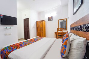 Een slaapkamer met een bed, een houten garderobe, een bureau, een stoel, een aan de muur bevestigde televisie en een lijst met een afbeelding.