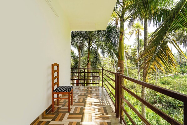 A balcony with a patterned floor, a wooden chair, and a railing overlooking a lush green landscape with palm trees. - Fabhotel Star Inn Plus - Near kovalam beach (Neyyattinkara)