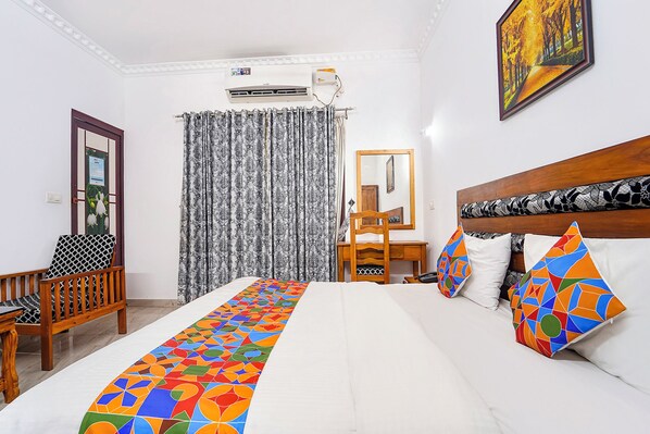 Habitación de hotel con cama, escritorio, silla, espejo y un cuadro en la pared.