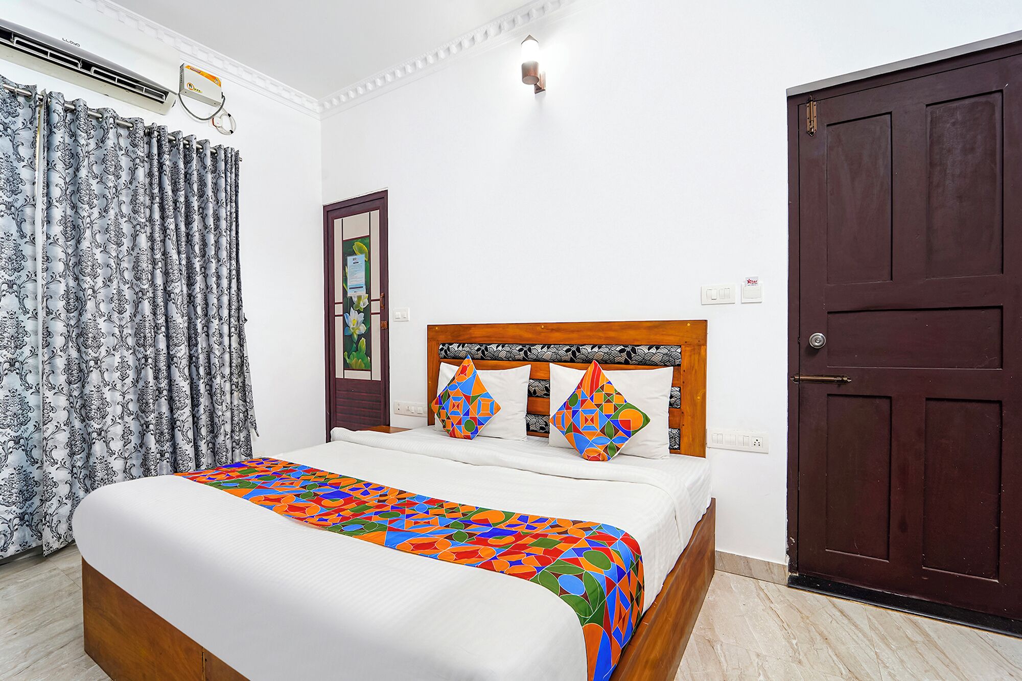 Un dormitorio con cama, cabecera de madera, puerta color café oscuro y ventana con cortinas.