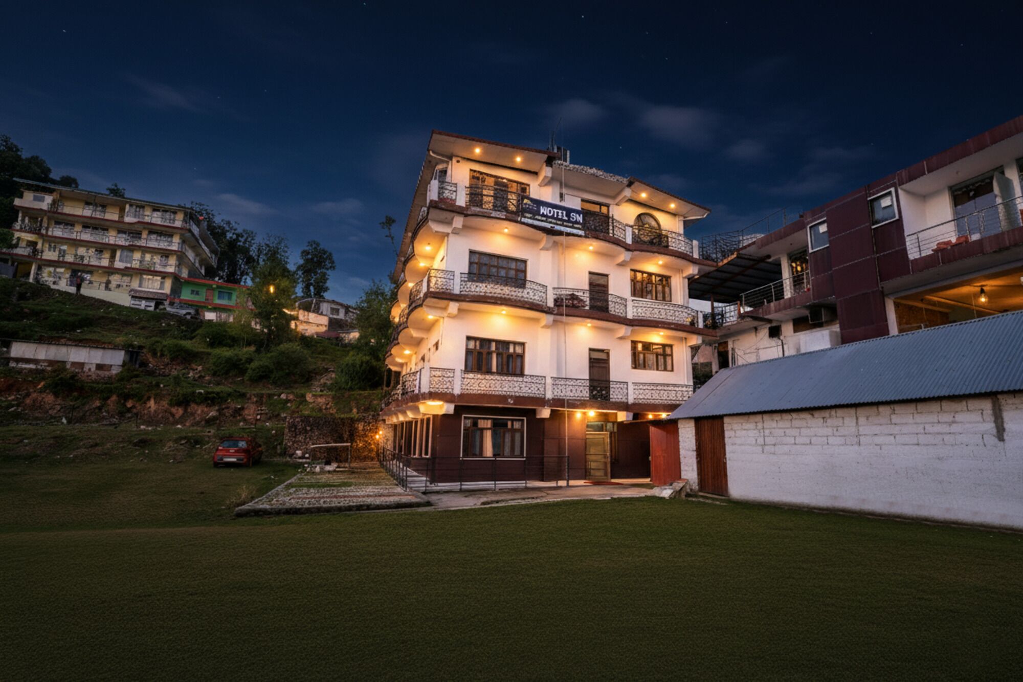 A multi-story hotel with balconies, a well-maintained lawn, and a clear night sky.