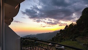 A balcony with a wrought iron railing overlooking a mountainous landscape during sunset. - Fabhotel Sn Resort (Dharamshala)