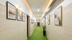A hallway with green carpet, framed artwork on the walls, and a potted plant. - Fabhotel Sn Resort (Dharamshala)