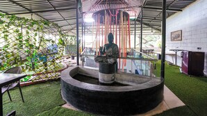 A statue in a circular stone basin under a metal roof with a white brick wall and a framed picture on the right. - Fabhotel Mazzo Residency (Nagaon)
