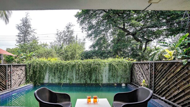 A pool area with two chairs and a table, surrounded by a bamboo fence and lush greenery. - Fabhotel Mazzo Residency (Nagaon)