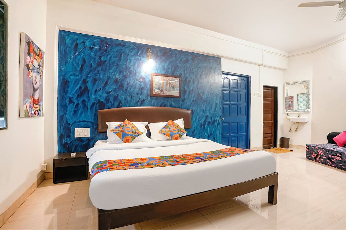 A bedroom with a bed, a blue door, a white wall, and a painting.