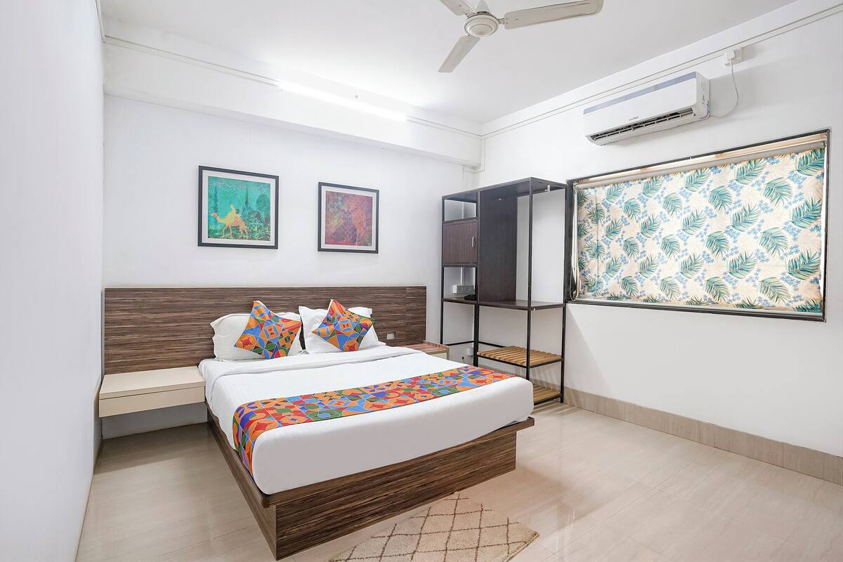 A bedroom with a bed, a wardrobe, a desk, and two framed artworks on the wall.