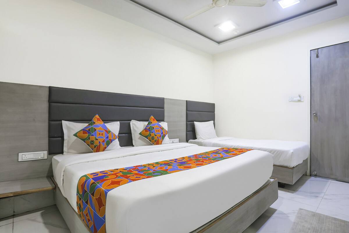 A hotel room with a large bed, two smaller beds, a grey headboard, and a wooden door.