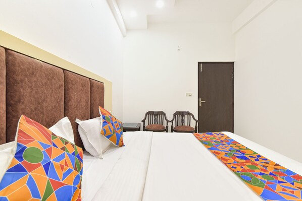 A hotel room with a large bed, two chairs, a wooden door, and a white wall. - Fabhotel Pearl (Haridwar)