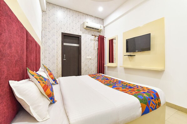 A hotel room with a bed, a TV mounted on the wall, and an air conditioning unit on the wall.