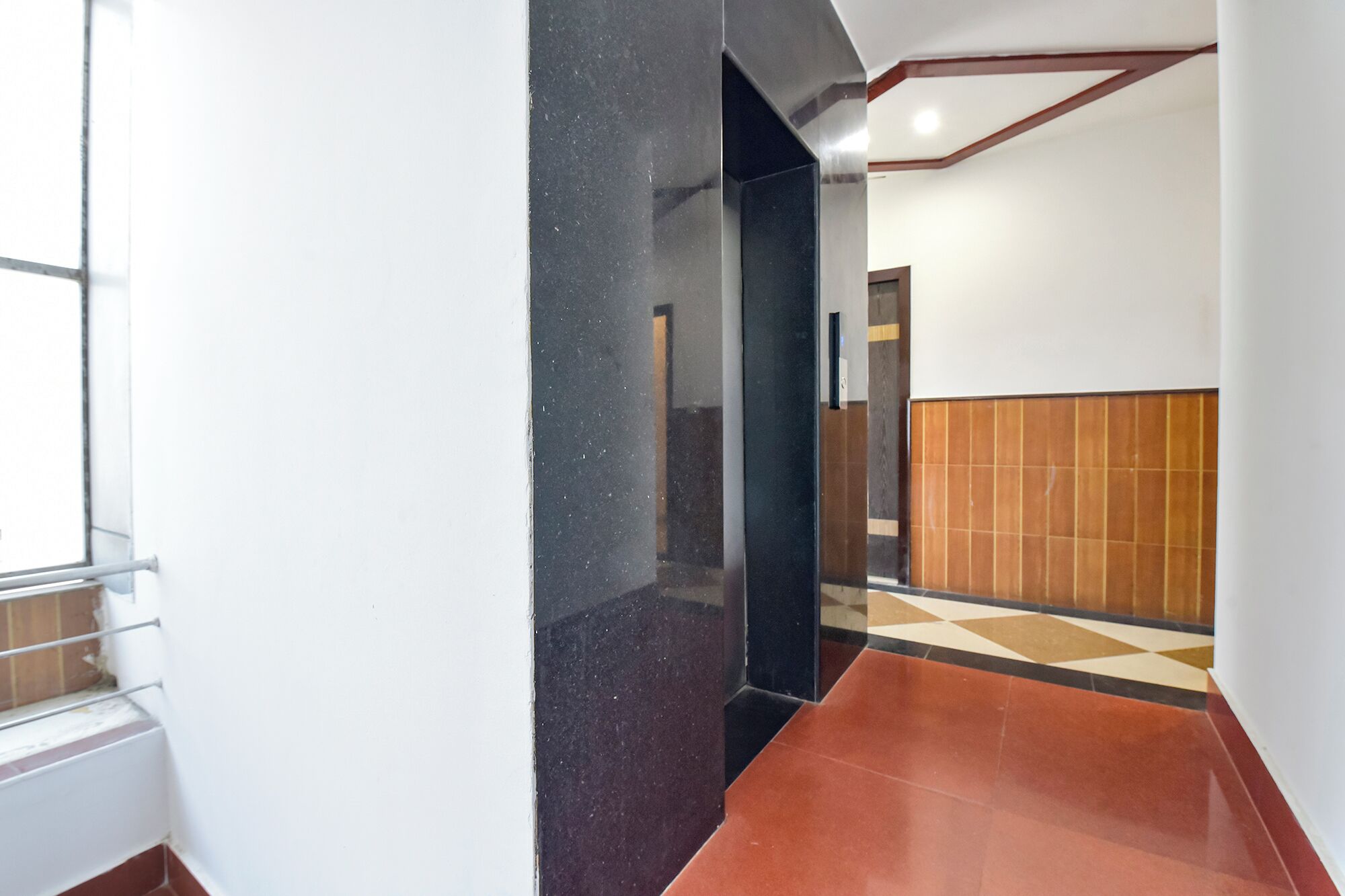 A hallway with a black marble wall, a wooden panel wall, and a tiled floor.