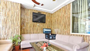 A modern living room with a sectional sofa, a glass coffee table, and a flat-screen TV mounted on a bamboo-patterned wall. - Fabhotel Pearl (Haridwar)