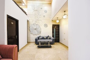 A modern interior with a sofa, a red chair, and decorative wall art. - Fabhotel Golden Key Inn (New Delhi)
