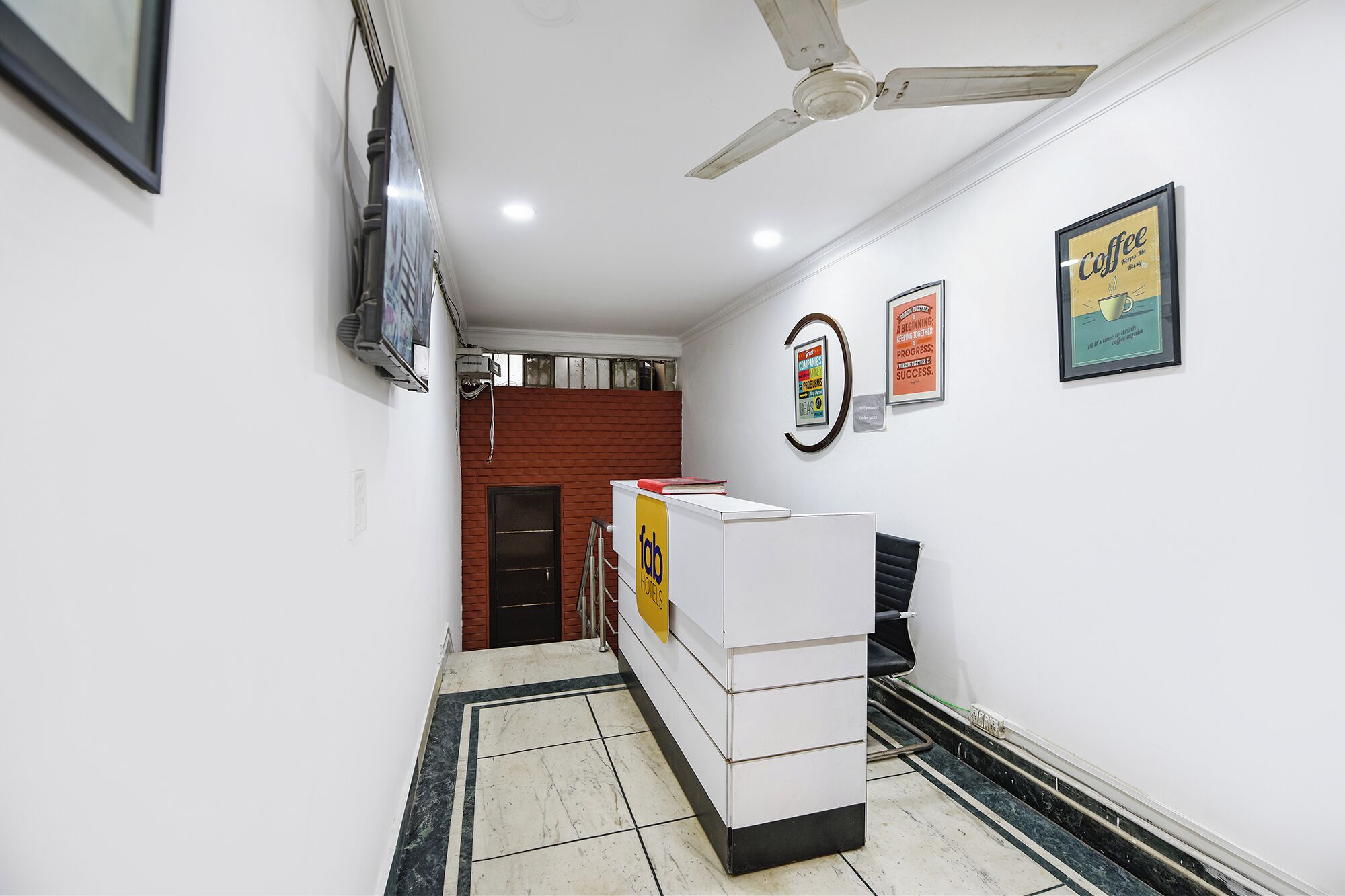 Un hall d’hôtel avec un comptoir d’accueil, un ventilateur de plafond et des affiches motivantes accrochées aux murs.