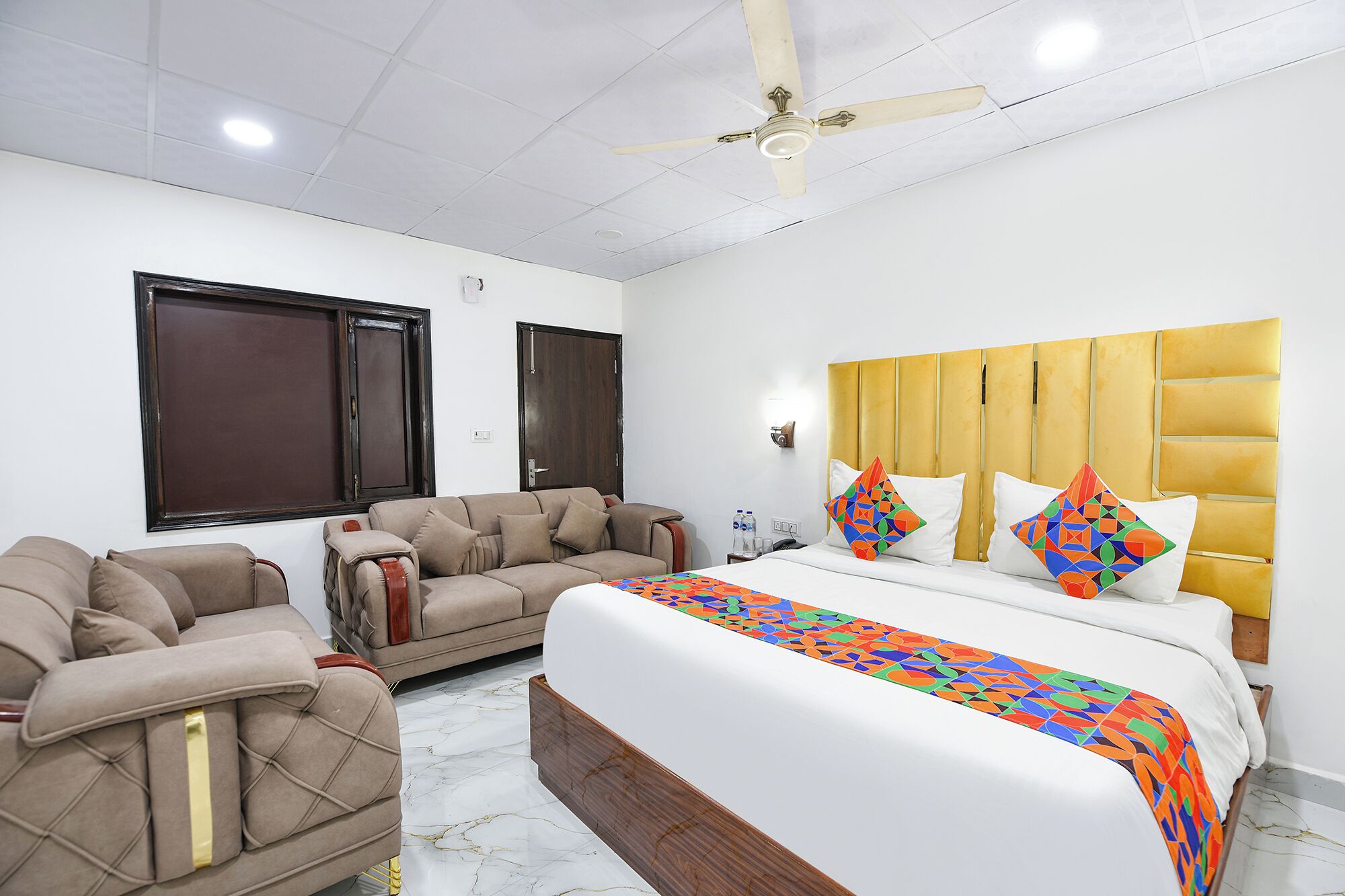 A hotel room with a bed, two sofas, a ceiling fan, and a window.