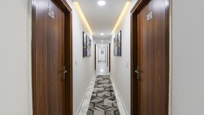 Een hotelgang met houten deuren, een kamerbreed tapijt met dessin en ingelijste foto’s aan de wanden.