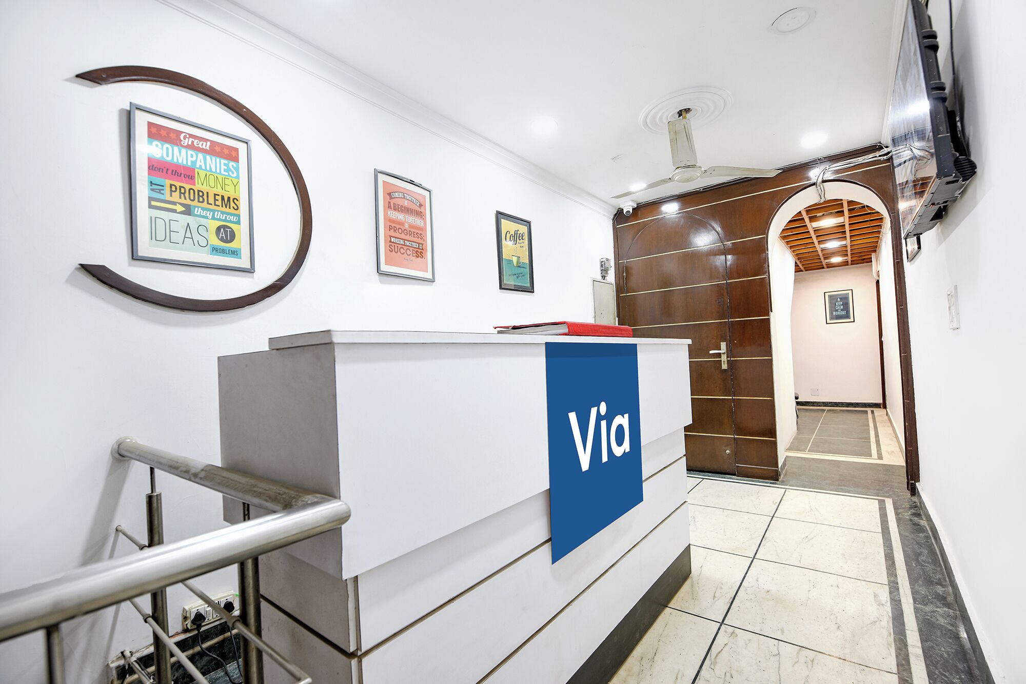 A reception desk with a 'Via' sign, a wall-mounted poster with motivational quotes, and a wooden door leading to another room.