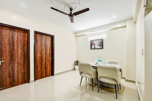 A hotel room with a wooden door, a ceiling fan, a dining table with chairs, and a framed picture on the wall. - Fabhotel The King Residency (New Delhi)