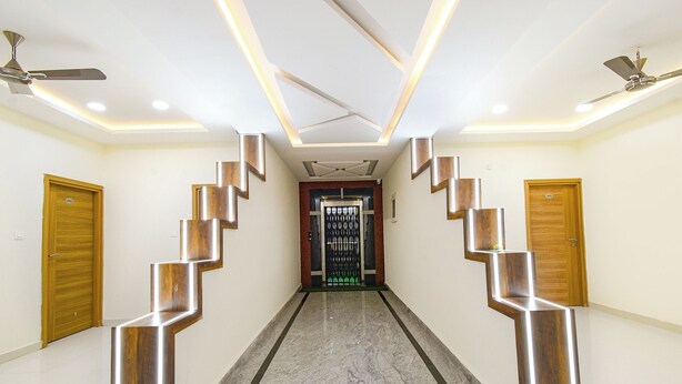 A modern hotel corridor with a central staircase, wooden doors, and ceiling fans. - Fabhotel Navya Grand (Hyderabad)