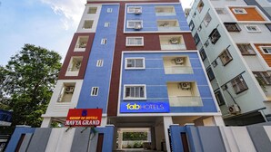 A multi-story hotel building with a blue and white facade, air conditioning units on each floor, and a sign for 'Group of Hotels Navya Grand'. - Fabhotel Navya Grand (Hyderabad)