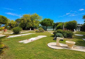 A well-maintained garden with a putting green, a small pond, and a variety of shrubs and trees.