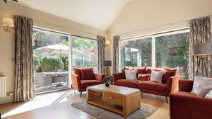 Ein geräumiges Wohnzimmer mit einer großen Couchgarnitur, einem Couchtisch und Blick ins Freie durch große Fenster.