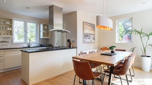 Eine moderne Küche mit einer zentralen Kochinsel, einem Essbereich mit Holztisch und Ledersesseln sowie einem großen Fenster, das für natürliches Licht sorgt.