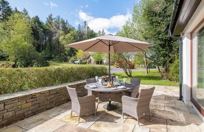 An outdoor patio with a round table, wicker chairs, and a large umbrella.