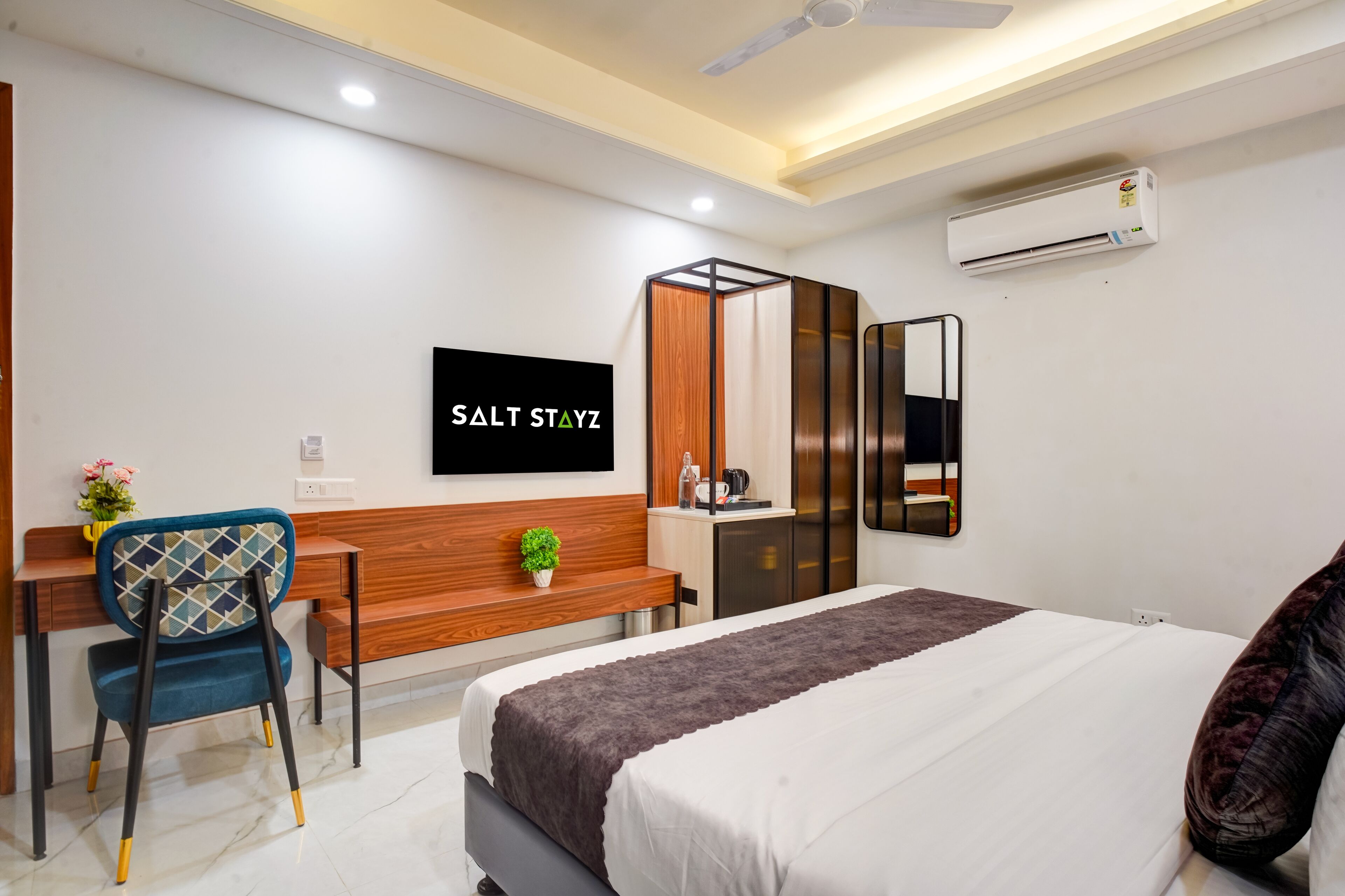 A modern hotel room with a bed, a desk, a chair, a TV, and an air conditioning unit.