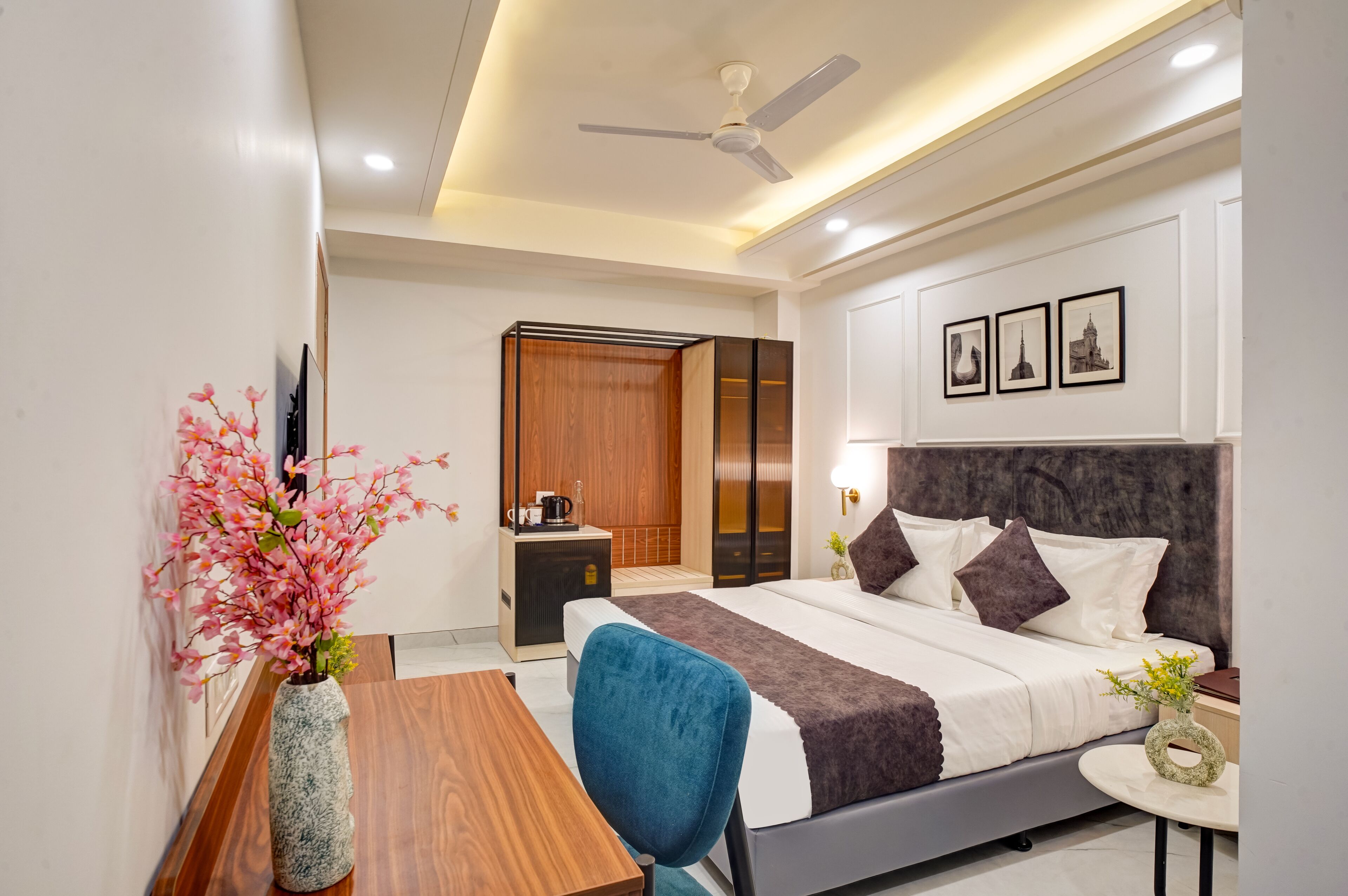 Une chambre d’hôtel moderne équipée d’un lit, d’un bureau, d’une chaise, d’une petite table et d’un vase avec des fleurs.