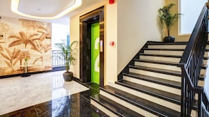 A modern hotel lobby with a marble floor, a staircase with black railings, and a green door. - Saltstayz Premier - Arjun Marg (Gurugram)