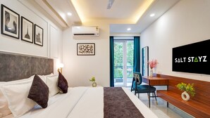 A modern hotel room with a bed, a desk, a TV, and a window with curtains. - Saltstayz Premier - Arjun Marg (Gurugram)