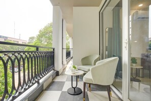A balcony with a checkered floor, two white chairs, a small table, and a potted plant. - Saltstayz Premier - Arjun Marg (Gurugram)