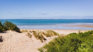 A beach with clear blue water, sandy shore, and green vegetation. - Sky Views by Property Mums (Somers)