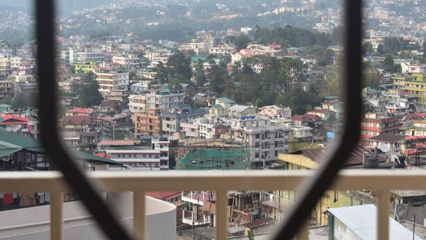 A cityscape viewed from a balcony with a railing in the foreground. - Elysian Home (Shillong)