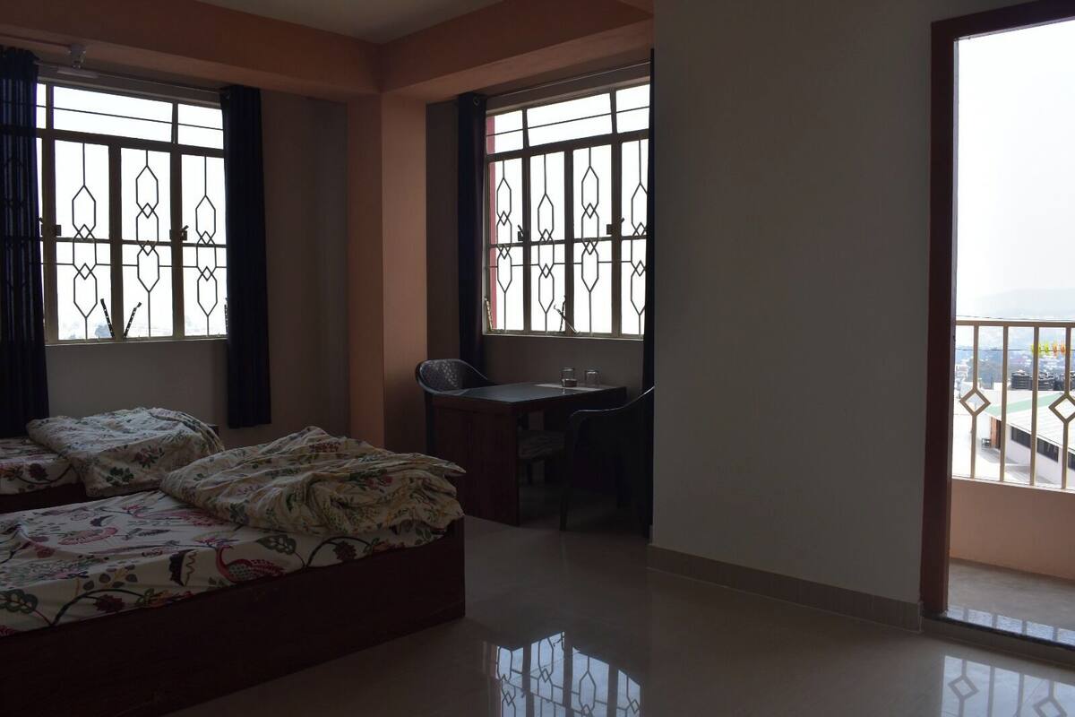 A room with two beds, a desk, and a balcony with a railing.