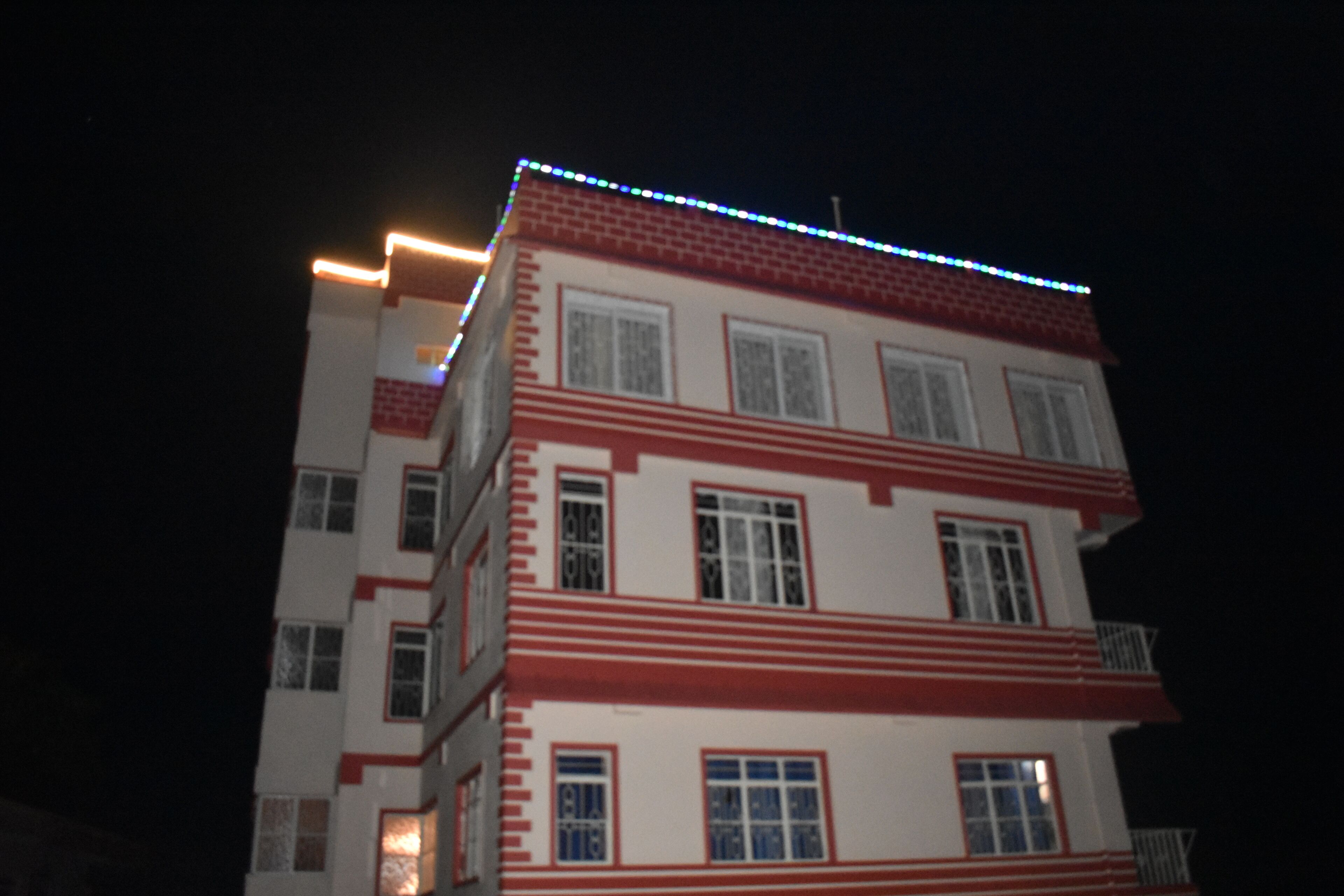A multi-story building with a red and white facade, multiple windows, and a balcony on the upper floors.