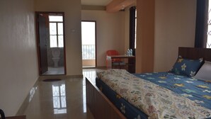A bedroom with a bed, a desk, and a bathroom with a toilet and sink. - Elysian Home (Shillong)
