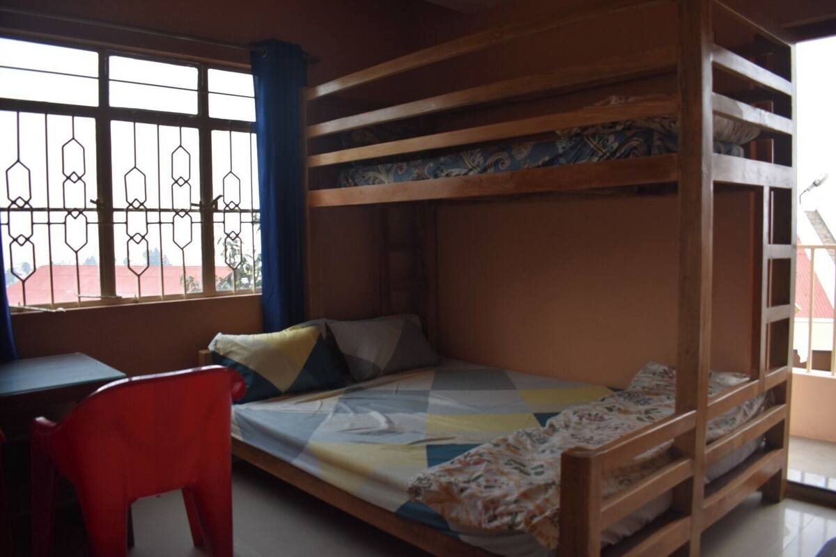 A bunk bed room with a desk and chair, a window with bars, and a view of the outside.