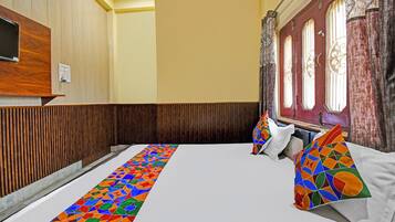 A hotel room with a wooden panel wall, a large bed with colorful pillows, and a window with curtains.