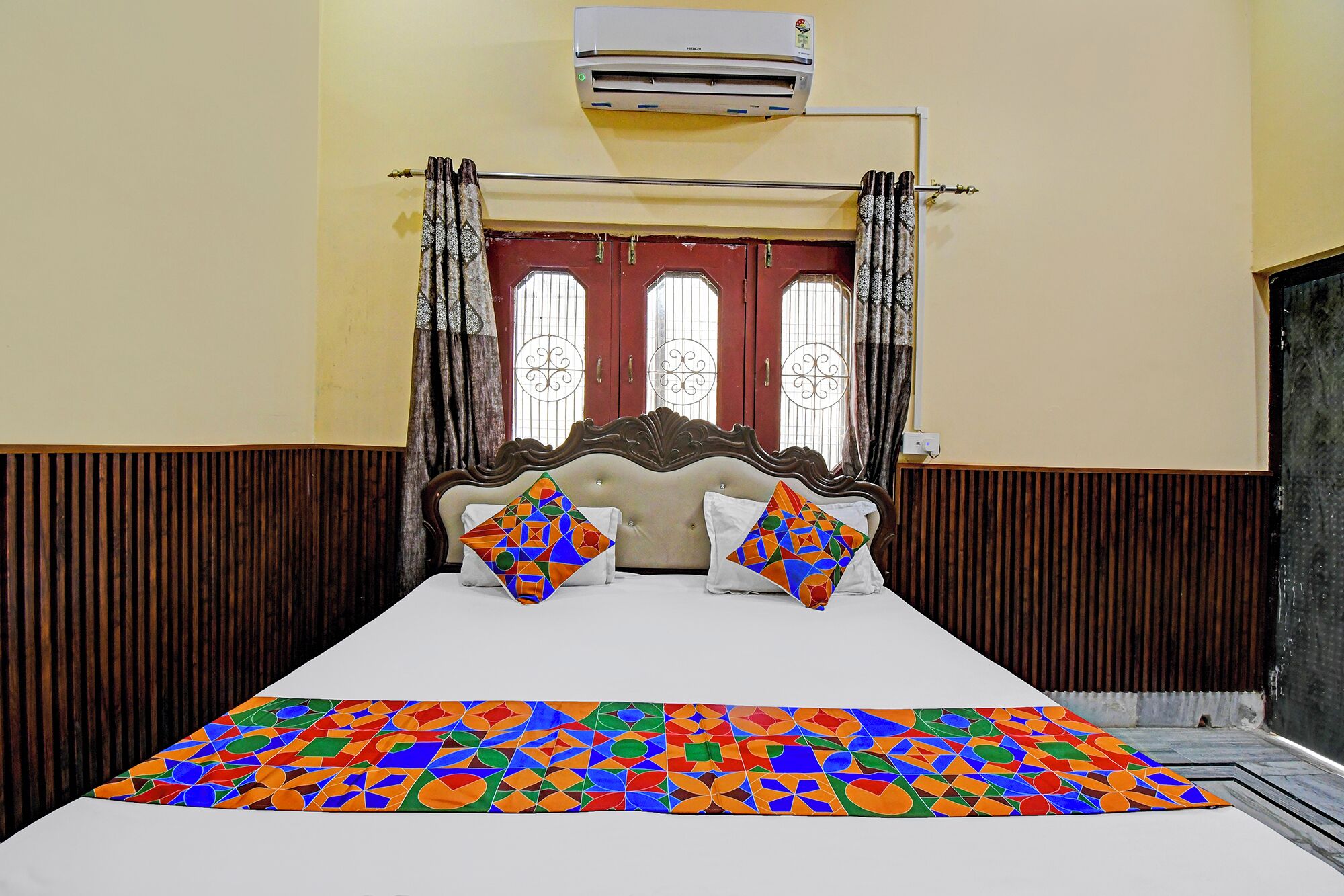 A bed with a patterned bedspread, a wooden headboard, and a window with decorative iron bars.