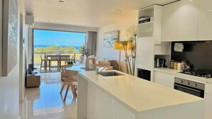 A modern kitchen with a large island, a dining area with a view, and a living space with a sofa and table. - Merewether By The Beaches Newcastle, Free Parking (Merewether)