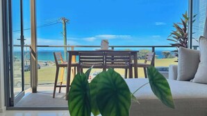 A modern living room with a large glass door leading to a balcony with a view of the ocean. - Merewether By The Beaches Newcastle, Free Parking (Merewether)