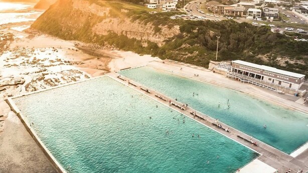 An aerial view of a coastal area with two large swimming pools, a building labeled 'Merewether Ocean Baths,' and a road with vehicles. - Merewether By The Beaches Newcastle, Free Parking (Merewether)
