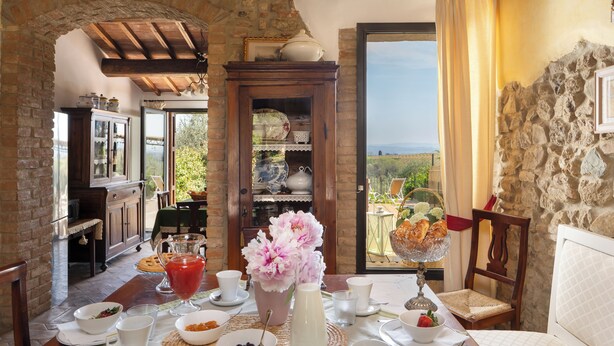 A dining area with a table set for breakfast, a stone archway, and a view of the outdoors. - L'antica Meletta (Gambassi Terme)