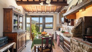 A rustic kitchen with wooden beams, a stone wall, and a view through the open door. - L'antica Meletta (Gambassi Terme)