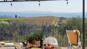 An outdoor dining area with a view of terraced fields, a table set with food and drinks, and a chair with a sun hat. - L'antica Meletta (Gambassi Terme)